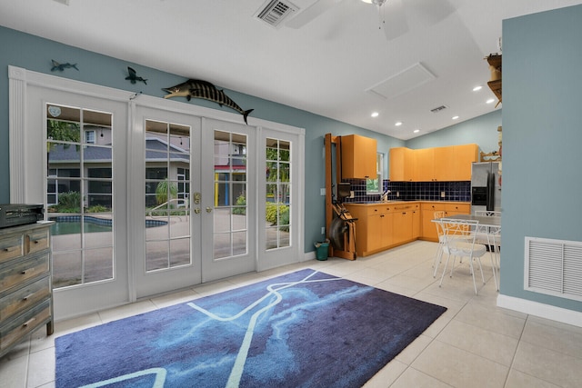 kitchen featuring vaulted ceiling, light tile patterned floors, french doors, backsplash, and stainless steel fridge