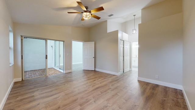 empty room with light wood-type flooring, ceiling fan, and high vaulted ceiling