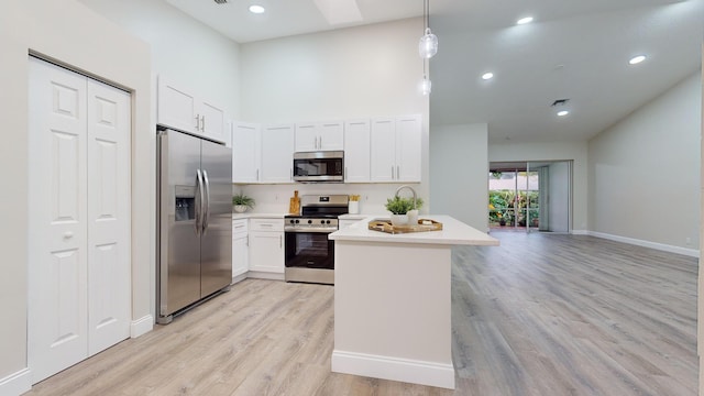 kitchen featuring white cabinets, decorative light fixtures, stainless steel appliances, light hardwood / wood-style floors, and kitchen peninsula