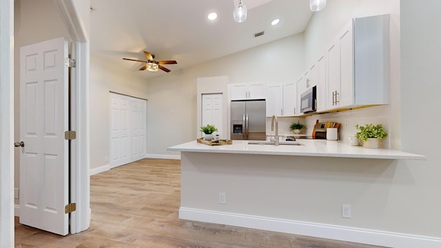 kitchen featuring kitchen peninsula, vaulted ceiling, appliances with stainless steel finishes, sink, and white cabinetry