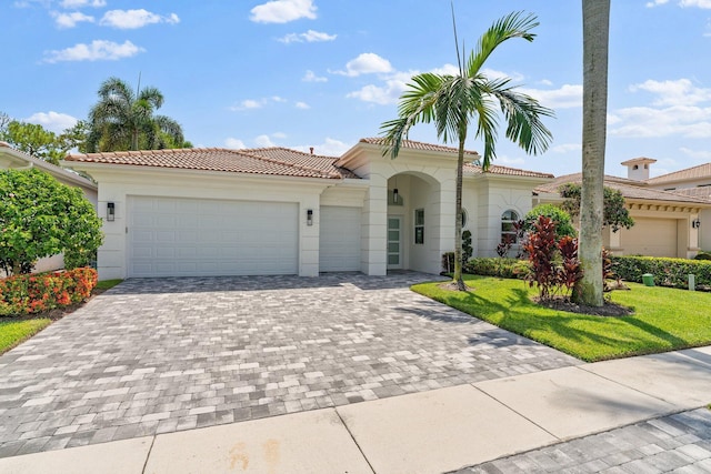 mediterranean / spanish house featuring a garage, a tile roof, decorative driveway, a front yard, and stucco siding