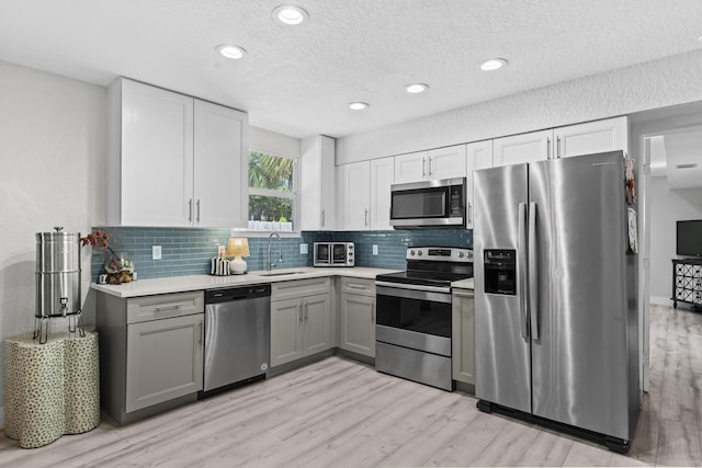 kitchen with stainless steel appliances, gray cabinets, sink, and backsplash