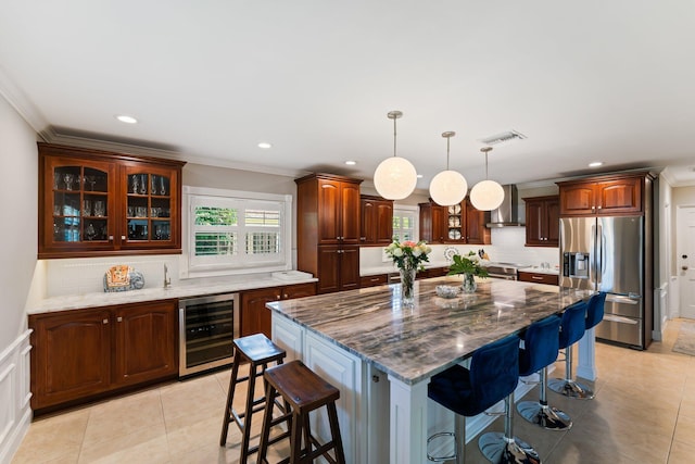 kitchen with hanging light fixtures, wall chimney exhaust hood, a center island, beverage cooler, and stainless steel appliances