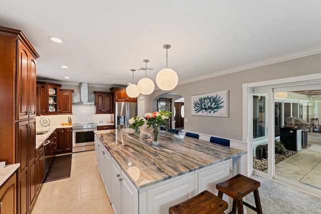 kitchen with appliances with stainless steel finishes, light tile patterned floors, a kitchen breakfast bar, wall chimney range hood, and a kitchen island