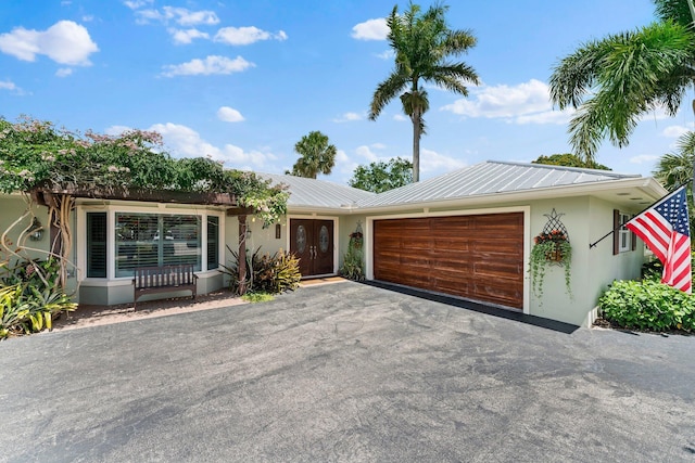 view of front facade with aphalt driveway, stucco siding, french doors, metal roof, and a garage