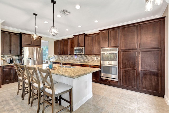 kitchen with sink, light stone counters, decorative light fixtures, appliances with stainless steel finishes, and an island with sink