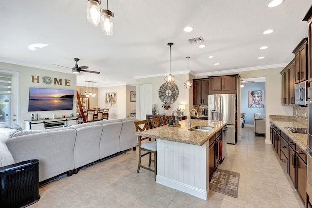 kitchen with appliances with stainless steel finishes, a center island with sink, light stone counters, a kitchen bar, and decorative light fixtures