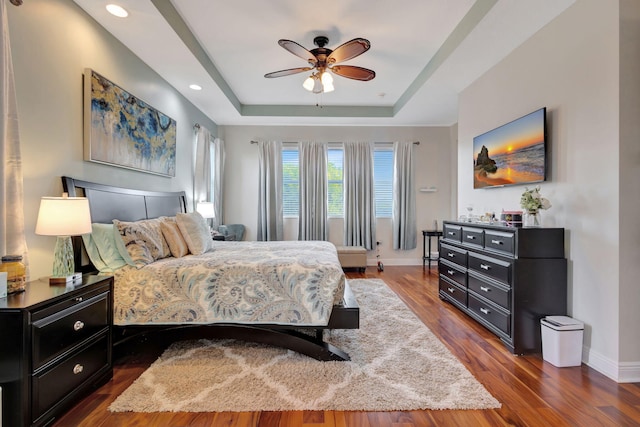 bedroom with dark wood-type flooring, a raised ceiling, and ceiling fan