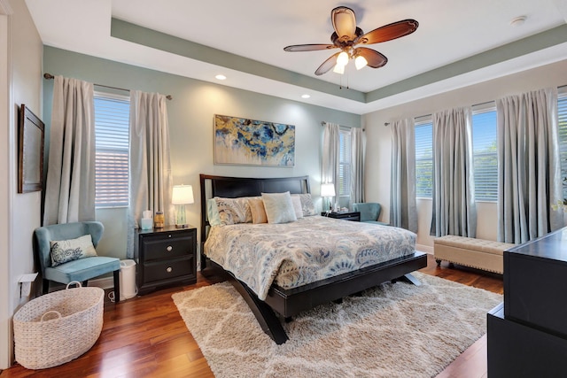 bedroom with hardwood / wood-style flooring, ceiling fan, and a tray ceiling