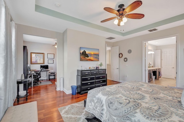 bedroom with ceiling fan, a tray ceiling, and hardwood / wood-style floors