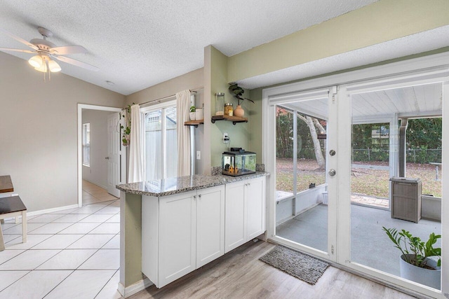 kitchen featuring light stone countertops, a textured ceiling, white cabinets, a wealth of natural light, and vaulted ceiling