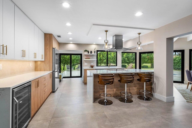 kitchen featuring wine cooler, stainless steel fridge, pendant lighting, island exhaust hood, and white cabinets