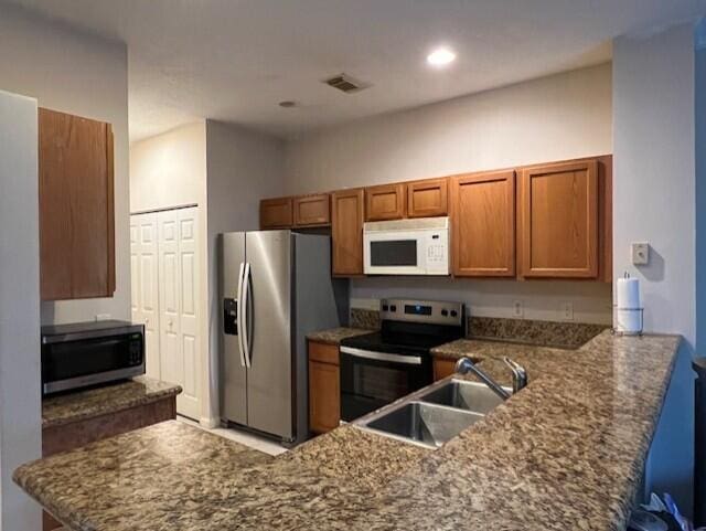 kitchen with sink, kitchen peninsula, stainless steel appliances, and dark stone counters