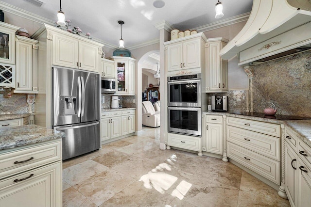 kitchen with appliances with stainless steel finishes, hanging light fixtures, light stone countertops, custom range hood, and cream cabinetry