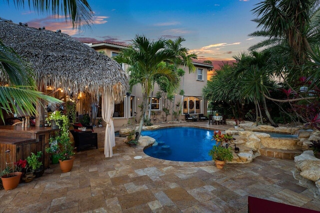 pool at dusk featuring an outdoor bar and a patio area