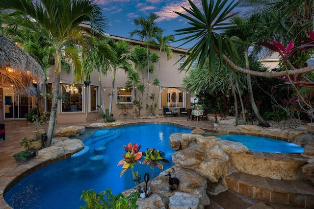 pool at dusk with an in ground hot tub and a patio area