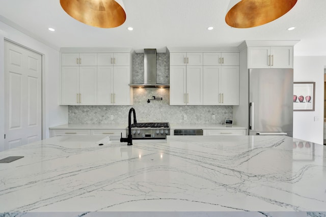 kitchen featuring white cabinetry, wall chimney exhaust hood, stainless steel fridge, and light stone countertops