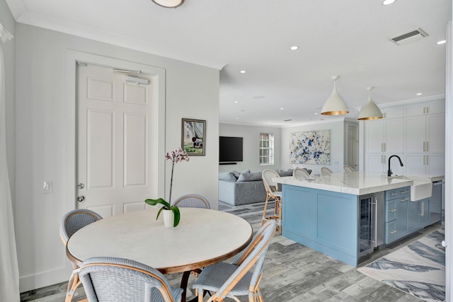 dining area with ornamental molding, beverage cooler, light hardwood / wood-style floors, and sink