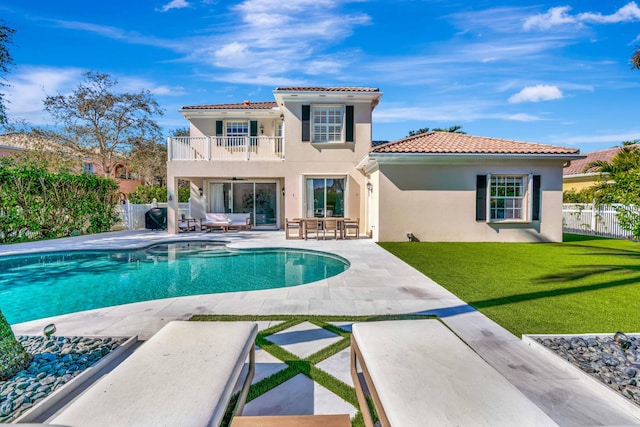 rear view of property featuring a fenced in pool, a patio, a balcony, and a yard