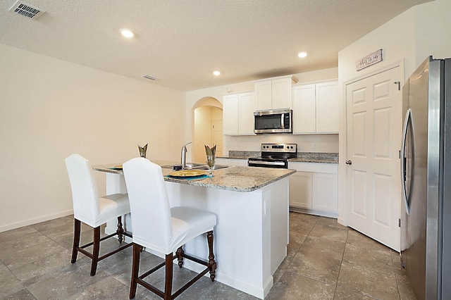 kitchen featuring white cabinets, stainless steel appliances, a kitchen island with sink, and a kitchen bar