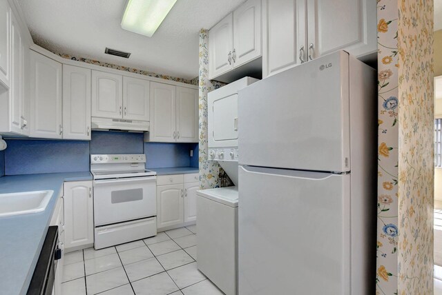 kitchen with stacked washer and dryer, sink, white cabinetry, light tile patterned floors, and white appliances
