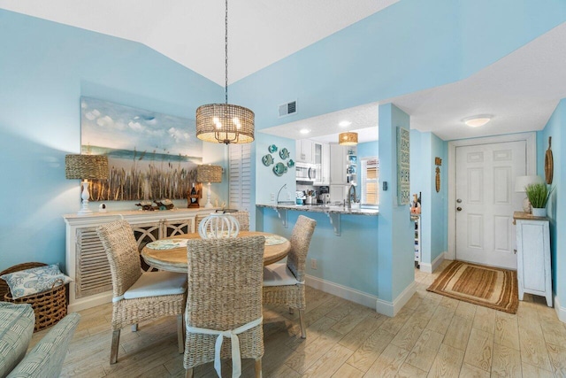 dining area featuring sink, light hardwood / wood-style flooring, and lofted ceiling