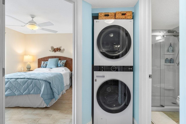 laundry area with ceiling fan, a textured ceiling, stacked washer / drying machine, and light hardwood / wood-style flooring