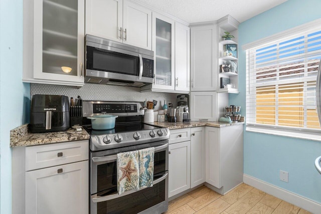 kitchen featuring white cabinetry, light stone counters, appliances with stainless steel finishes, and decorative backsplash