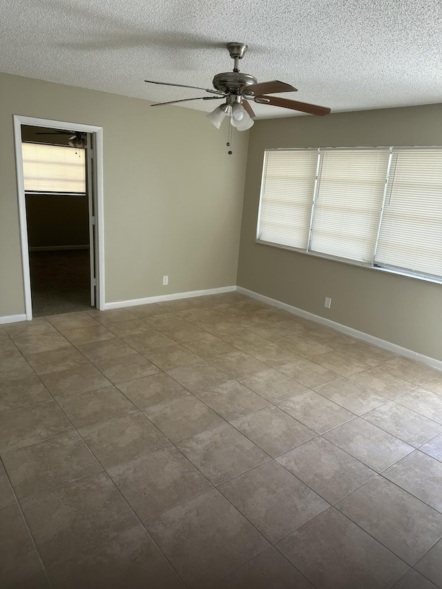 tiled empty room with baseboards, a textured ceiling, and a ceiling fan