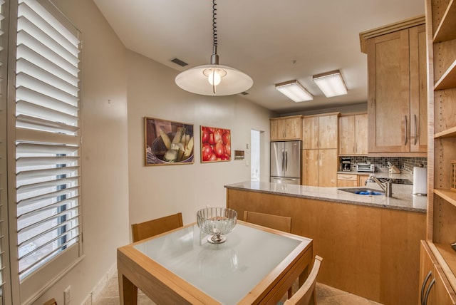 kitchen with sink, stainless steel fridge, hanging light fixtures, backsplash, and kitchen peninsula