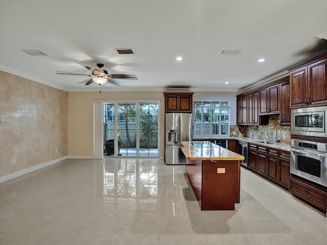 kitchen with a kitchen island, sink, light stone counters, stainless steel appliances, and crown molding