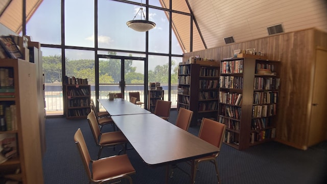 office area with dark carpet, a towering ceiling, floor to ceiling windows, wood ceiling, and wood walls