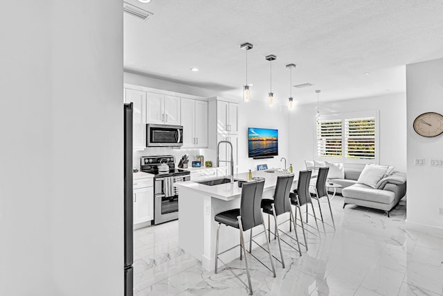 kitchen with white cabinets, stainless steel appliances, sink, a center island with sink, and a breakfast bar area