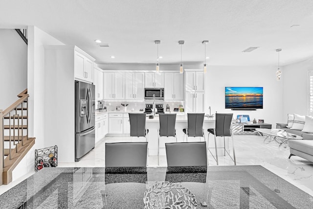 kitchen featuring decorative light fixtures, white cabinets, appliances with stainless steel finishes, and a kitchen island with sink