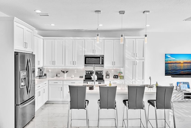 kitchen with stainless steel appliances, white cabinetry, a kitchen island with sink, and decorative light fixtures