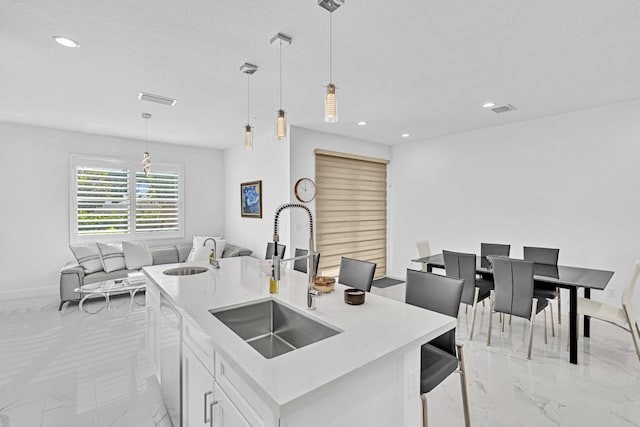 kitchen with sink, white cabinets, a kitchen island with sink, and hanging light fixtures