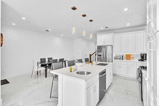 kitchen featuring white cabinets, hanging light fixtures, a center island with sink, and appliances with stainless steel finishes