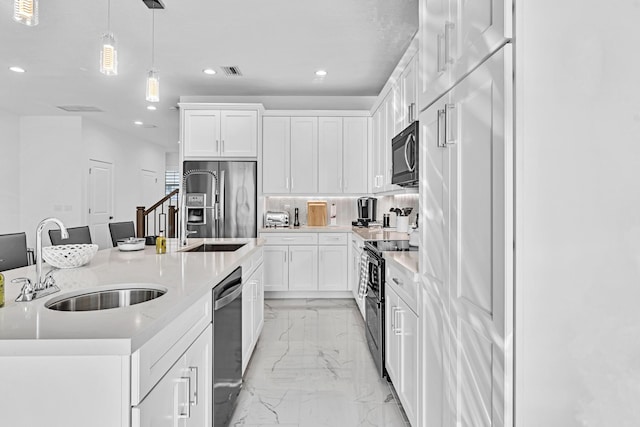 kitchen with white cabinets, appliances with stainless steel finishes, decorative light fixtures, sink, and a center island with sink