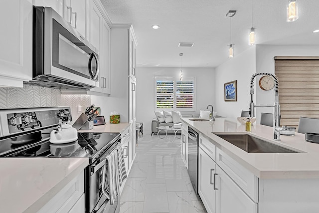 kitchen with sink, white cabinets, hanging light fixtures, and appliances with stainless steel finishes