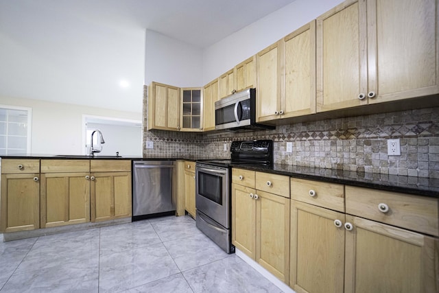 kitchen with appliances with stainless steel finishes, tasteful backsplash, sink, dark stone countertops, and light brown cabinets