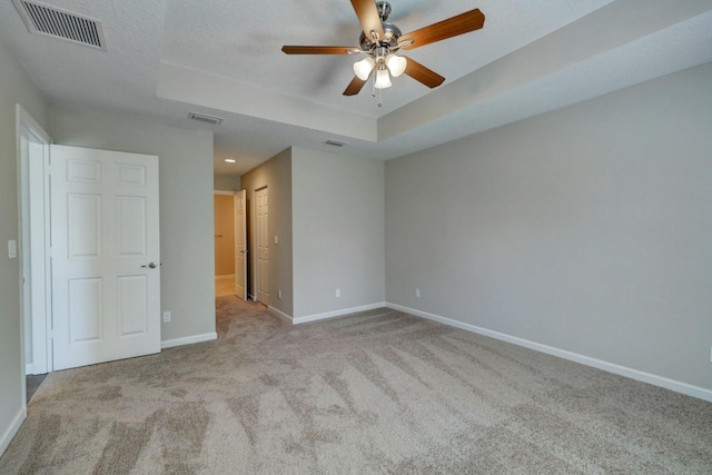 unfurnished bedroom featuring light carpet, a textured ceiling, ceiling fan, and a tray ceiling