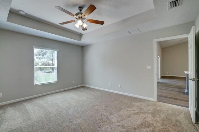 unfurnished room with ceiling fan, a tray ceiling, carpet floors, and a textured ceiling