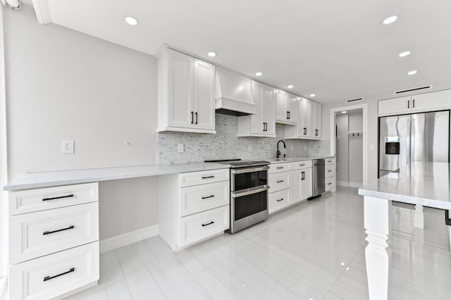 kitchen with white cabinets, backsplash, stainless steel appliances, light stone countertops, and wall chimney range hood