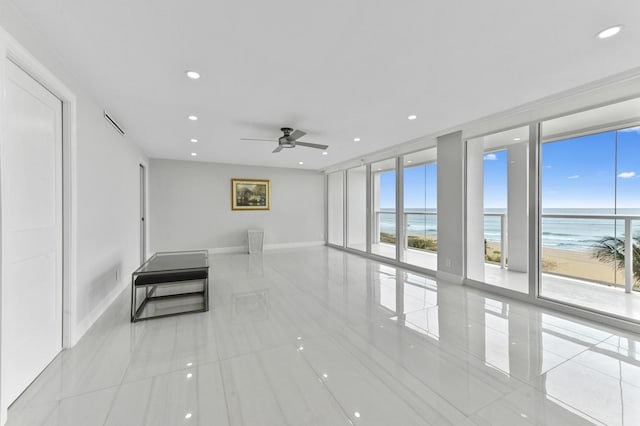 unfurnished living room with a view of the beach, light tile patterned floors, a wall of windows, ceiling fan, and a water view