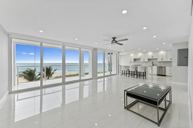 tiled living room featuring sink, ceiling fan, floor to ceiling windows, a water view, and a beach view