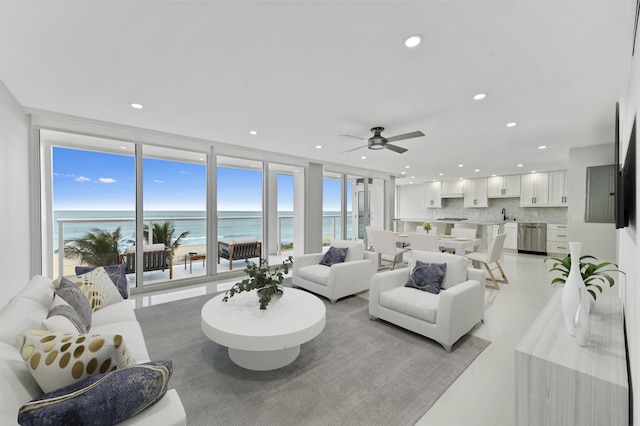 living room with a view of the beach, light tile patterned floors, ceiling fan, floor to ceiling windows, and a water view