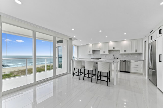 kitchen with appliances with stainless steel finishes, white cabinetry, a kitchen breakfast bar, a water view, and a beach view