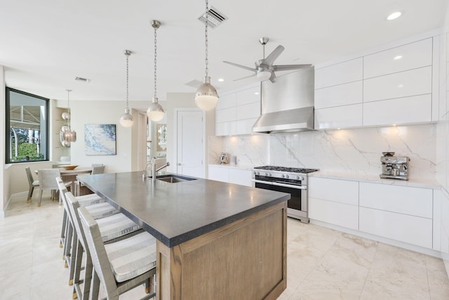 kitchen featuring white cabinetry, sink, double oven range, a kitchen island with sink, and wall chimney range hood