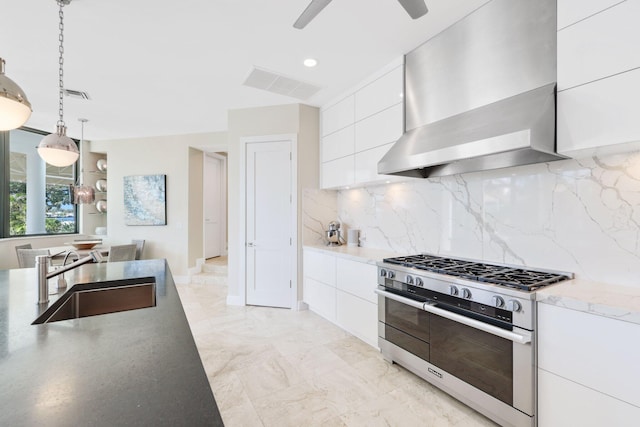 kitchen featuring pendant lighting, wall chimney range hood, sink, white cabinetry, and range with two ovens