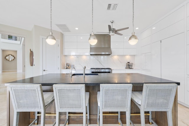 kitchen with stove, a kitchen island with sink, white cabinets, and wall chimney exhaust hood